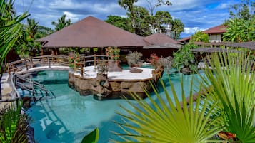 A tropical resort with a central pool, surrounded by lush greenery and covered seating areas.