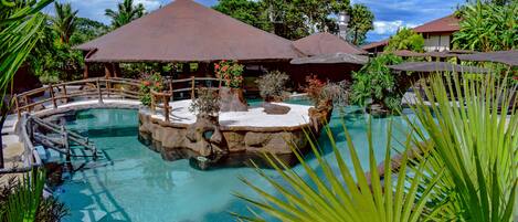 A tropical resort with a central pool, surrounded by lush greenery and covered seating areas.