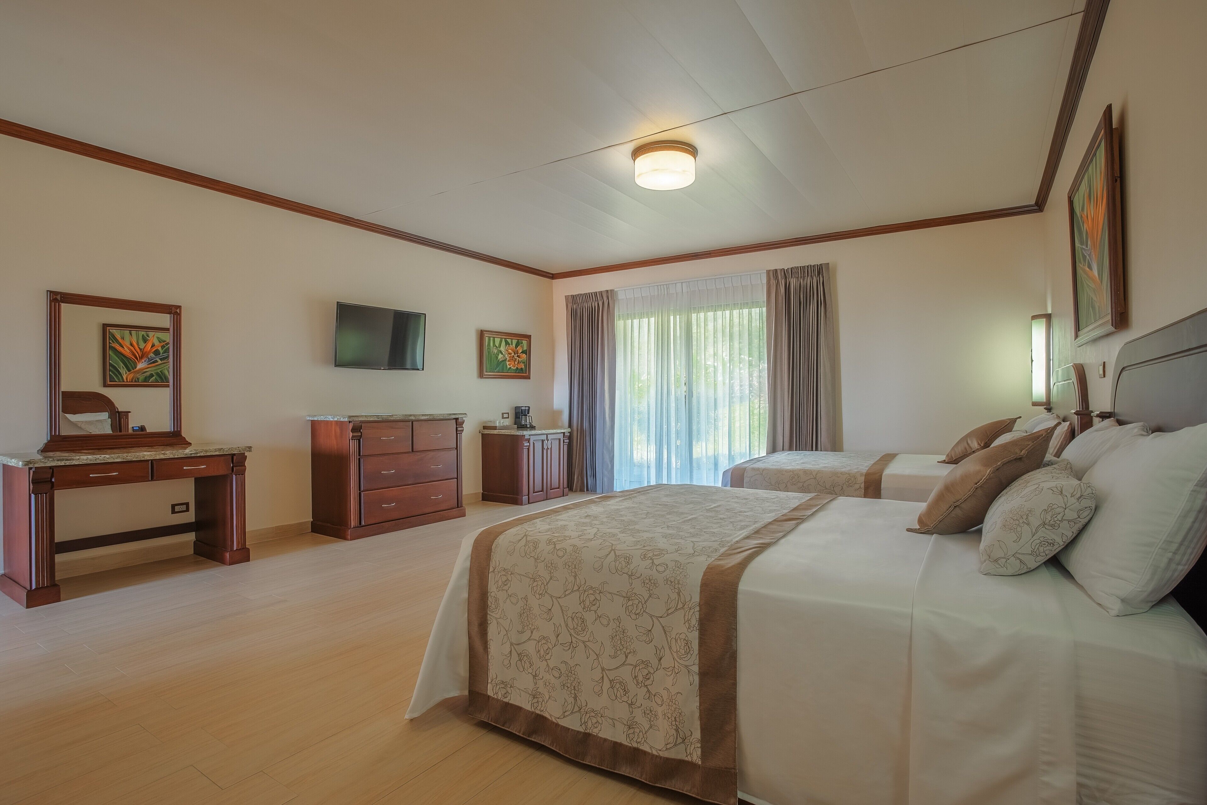 A hotel room with two beds, a desk, a dresser, a television, and a window with curtains.