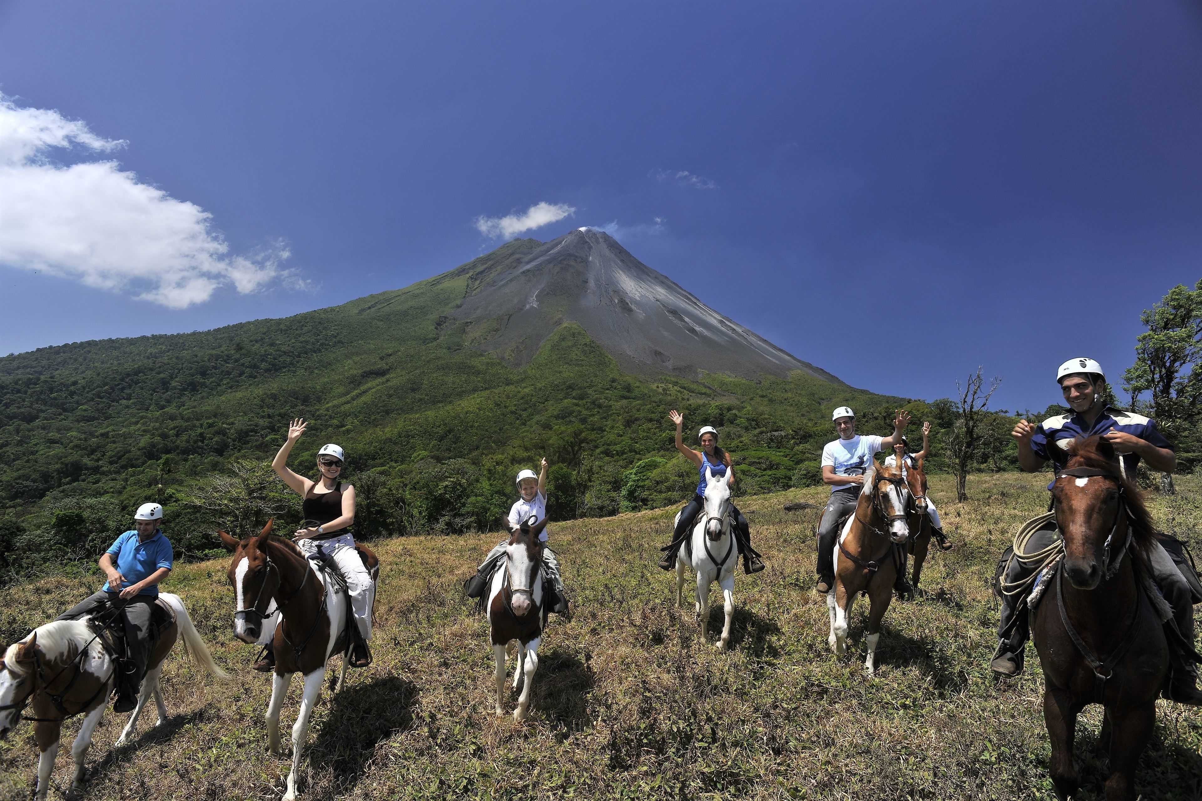 A group of people on horseback on a grassy field with a mountain in the background.
