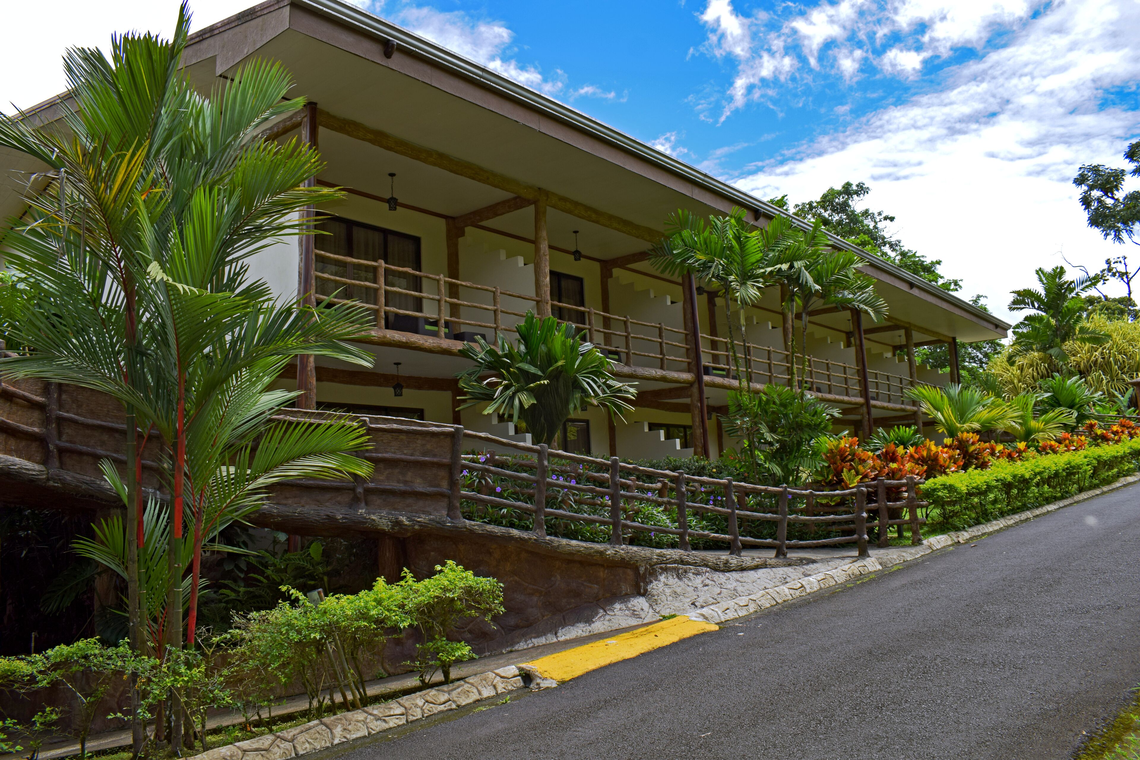 Un bâtiment à deux étages doté d’un balcon, entouré de plantes tropicales et d’un mur de pierre.
