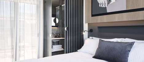 Una habitación de hotel moderna con una cama grande, un armario y vistas a través de un ventanal.