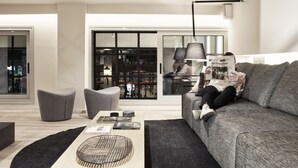 Un salón moderno con un sofá gris, una mesa de centro con libros y un ventanal con vistas a un paisaje urbano.