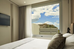 Et hotelværelse med en seng, et fladskærms-tv på væggen og et vindue med udsigt til en bygning og skyer.
