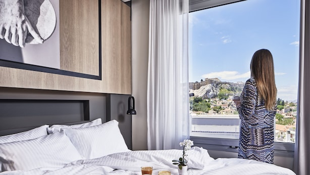 Habitación de hotel con cama, ventana con vistas a un paisaje urbano y bandeja con café y galletas.