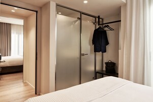 Una camera d'albergo con un letto, un armadio, un appendiabiti e un tavolino con una borsa.