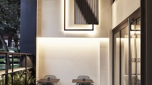 Un área de comedor al aire libre con mesas y sillas, una lámpara moderna y un muro de vidrio.
