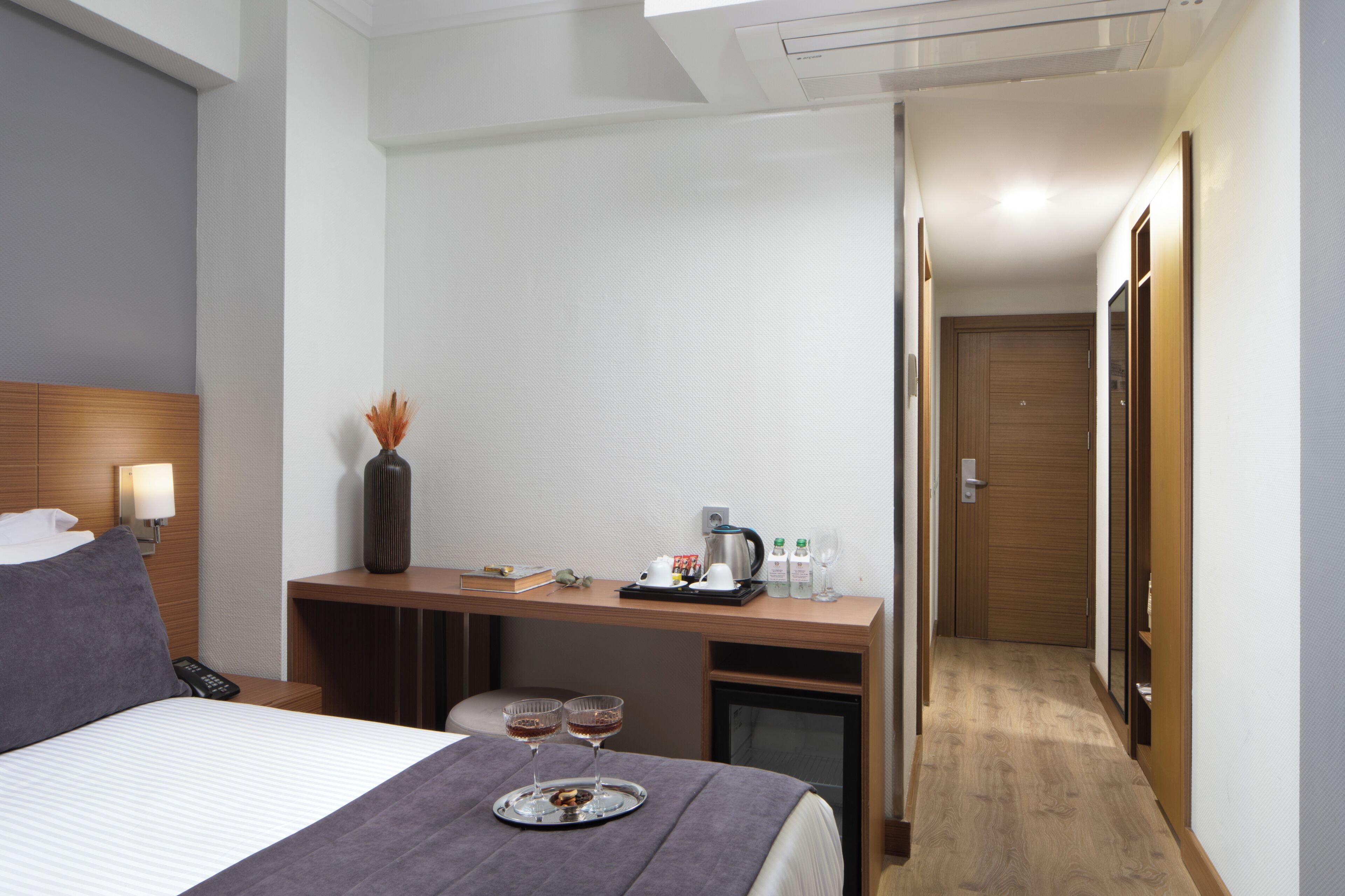 A hotel room with a bed, a desk, a coffee maker, two wine glasses, and a tray with snacks.