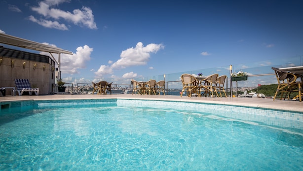 A clear blue pool with wicker chairs and a view of the city skyline. - Orka Royal Hotel & Spa (Istanbul)