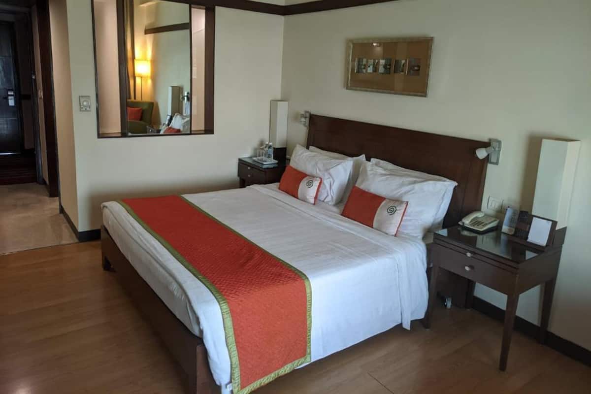 A hotel room with a large bed, a nightstand with a phone, a mirror, and a framed picture on the wall.
