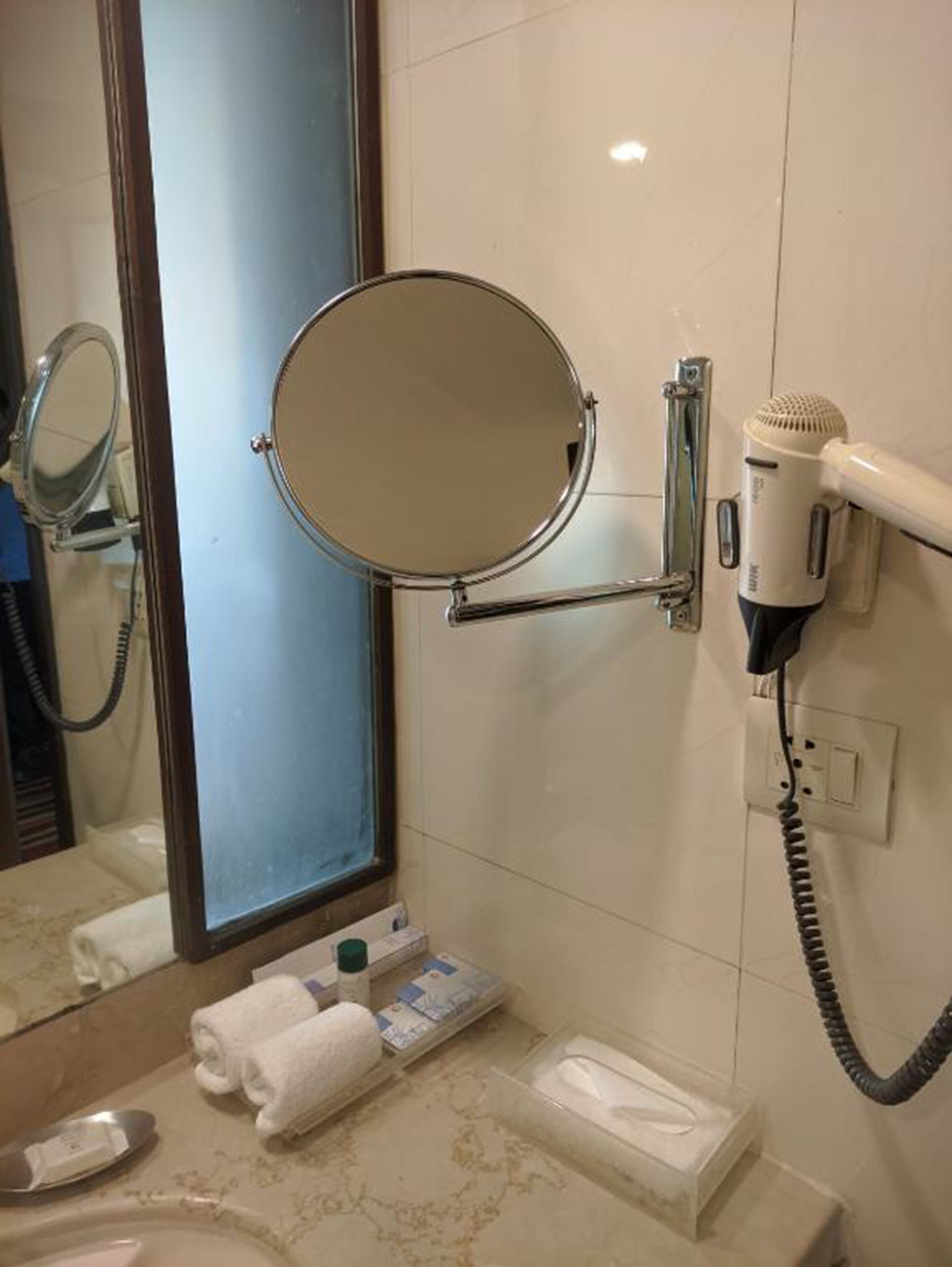 A bathroom with a mirror, a hairdryer, and toiletries on the counter.