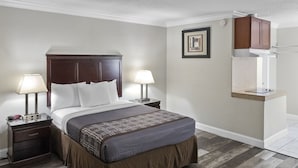 A hotel room with a large bed, two bedside tables, a nightstand, a built-in shelf, and a framed picture on the wall. - Dream Inn (Fresno)