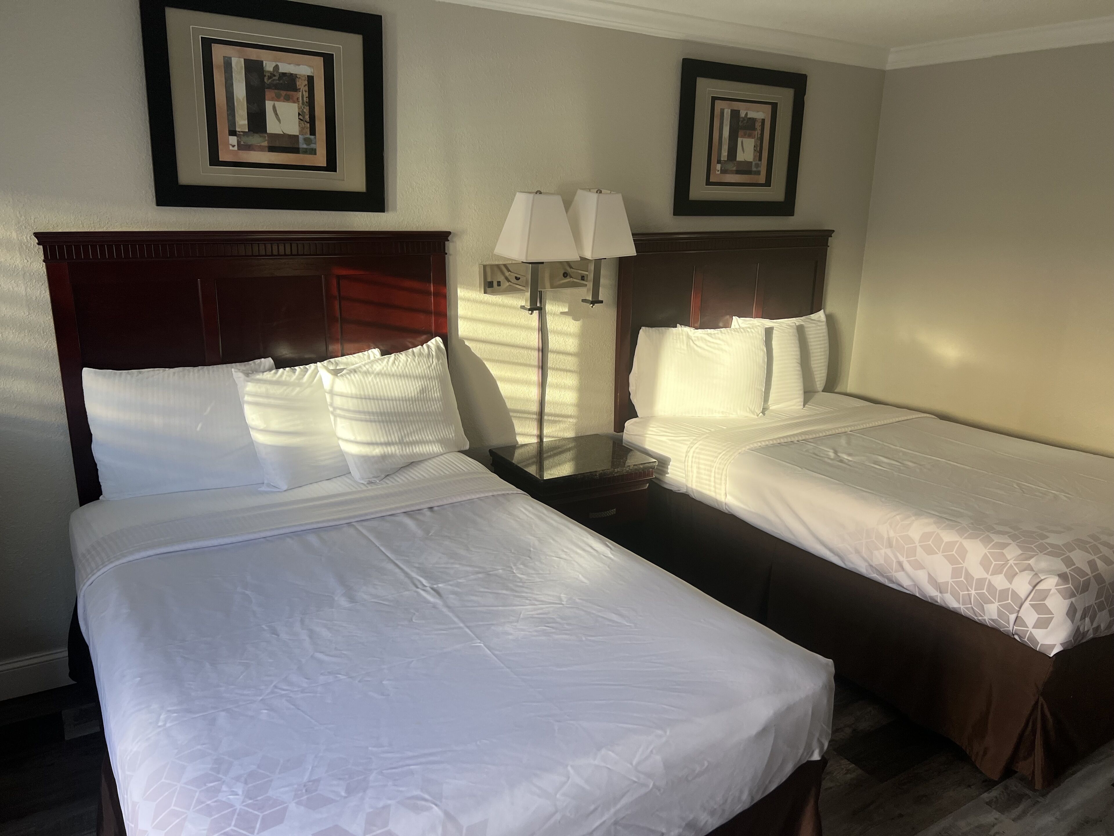 A hotel room with two beds, each with white bedding and a wooden headboard. There are two framed pictures on the wall above the beds.