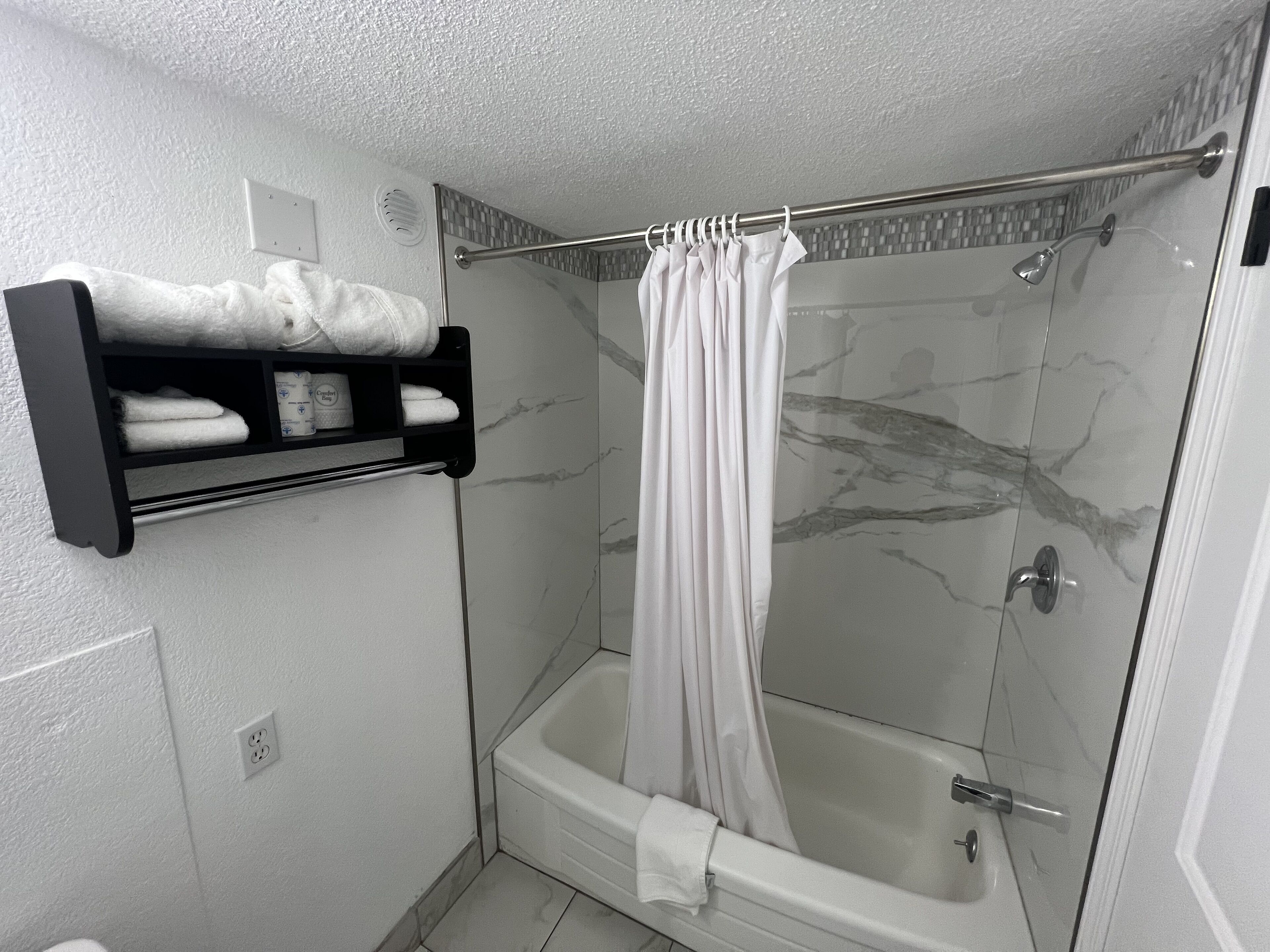 Un baño moderno con ducha de vidrio, una bañera blanca y un perchero con toallas dobladas con esmero.