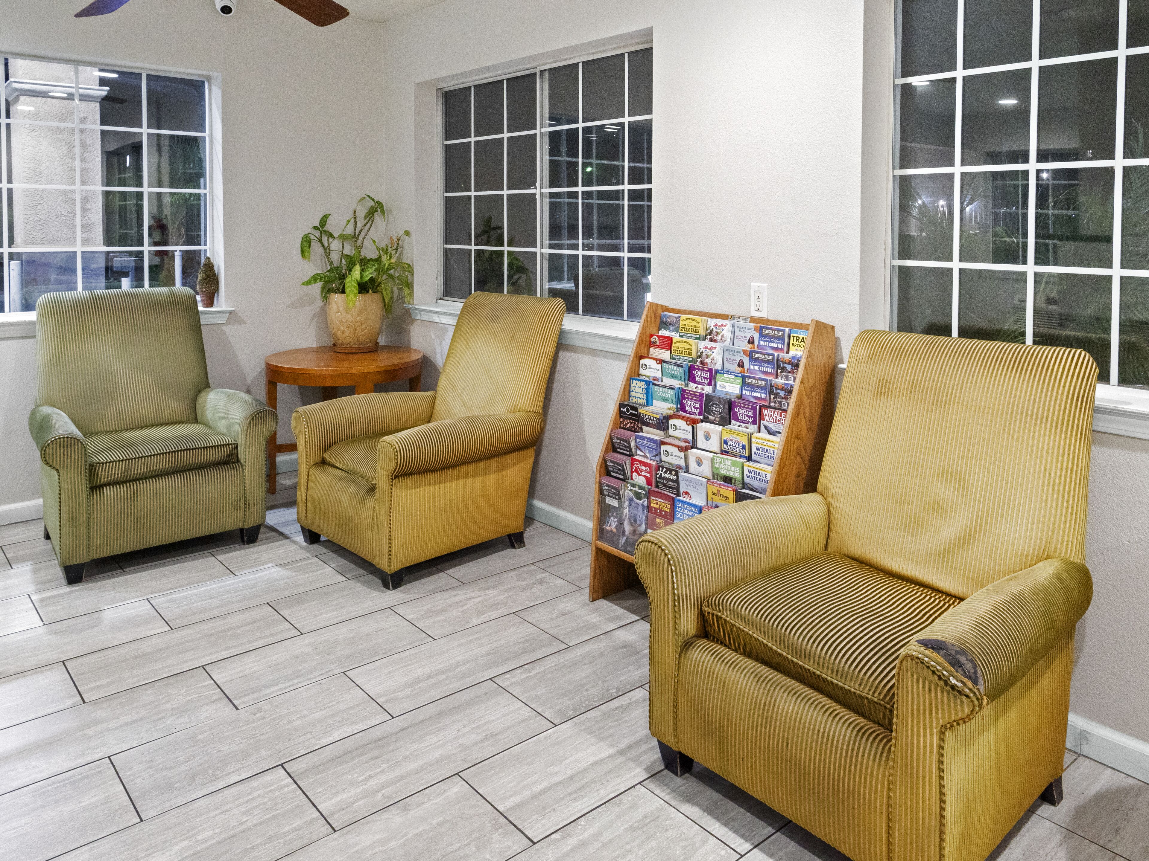 A room with three armchairs, a small table with a plant, and a bookshelf filled with books.