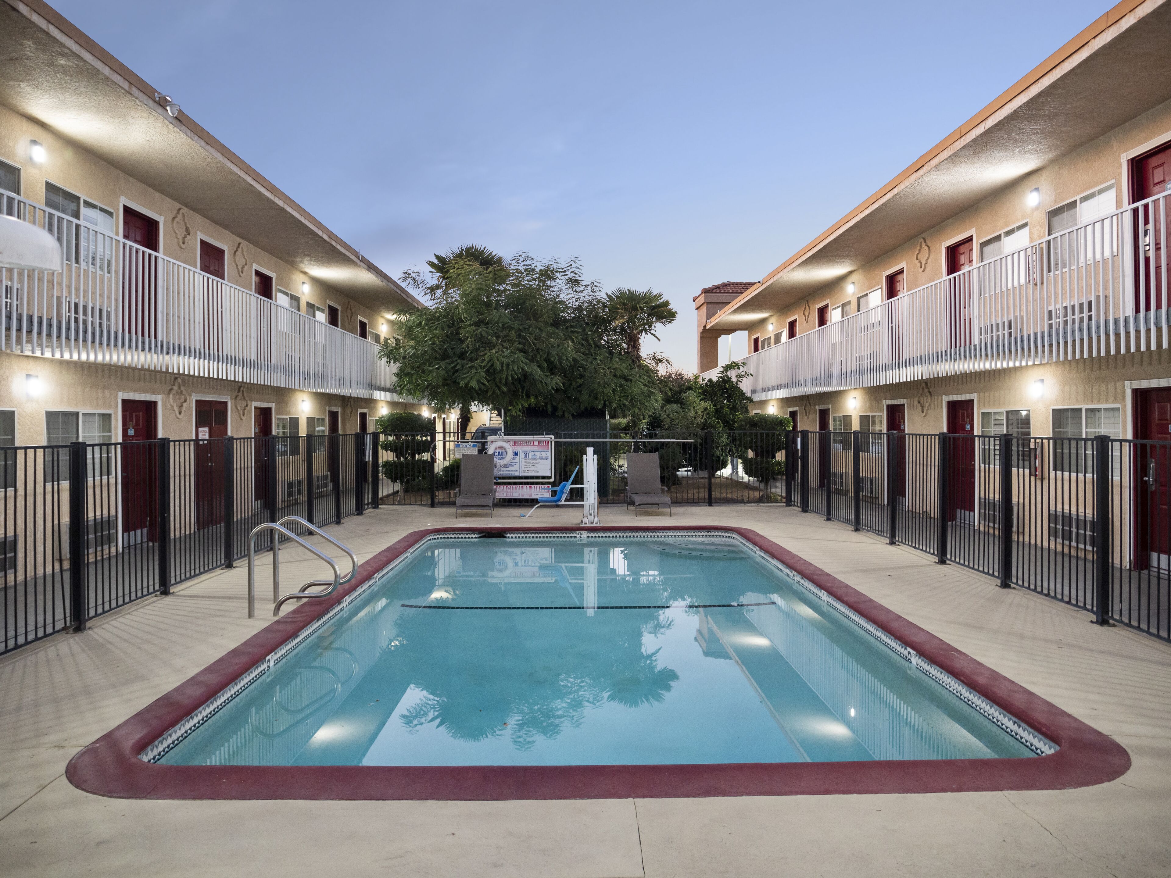 Une piscine entourée d’une zone délimitée par une clôture, avec un bâtiment en arrière-plan.