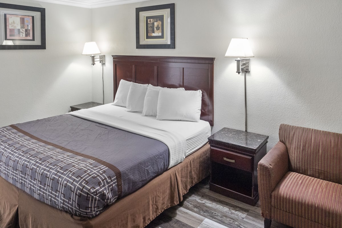 Ein Hotelzimmer mit einem großen Bett, zwei Nachttischen, einem Sessel und zwei Wandleuchten.