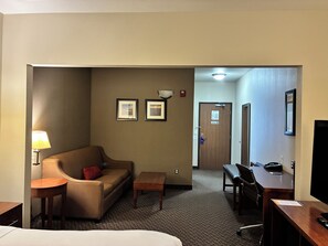 A hotel room with a bed, a sofa, a desk, a chair, a lamp, and two framed pictures on the wall.
