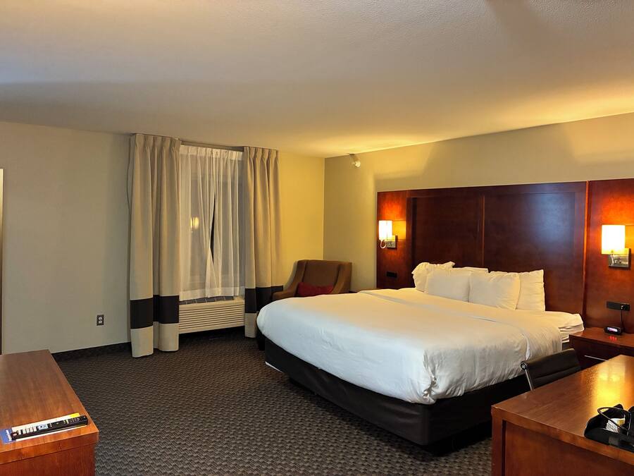 A hotel room with a large bed, a desk, a chair, and a wall-mounted lamp.