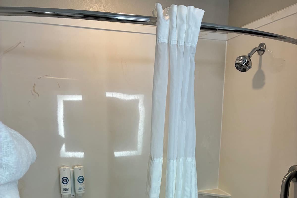 A glass-enclosed shower with a white curtain, a white towel, and two shampoo bottles on the wall.