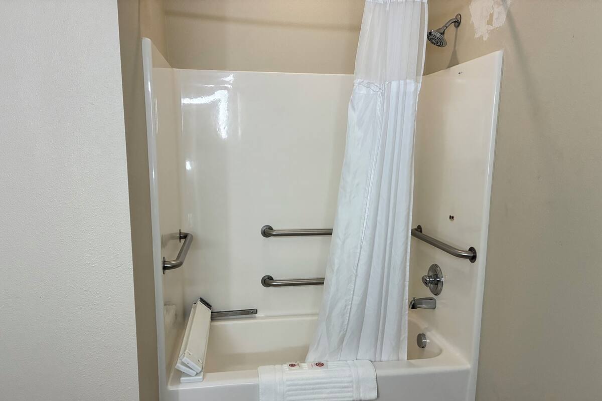 A bathtub with a white shower curtain, grab bars, and a towel rack.
