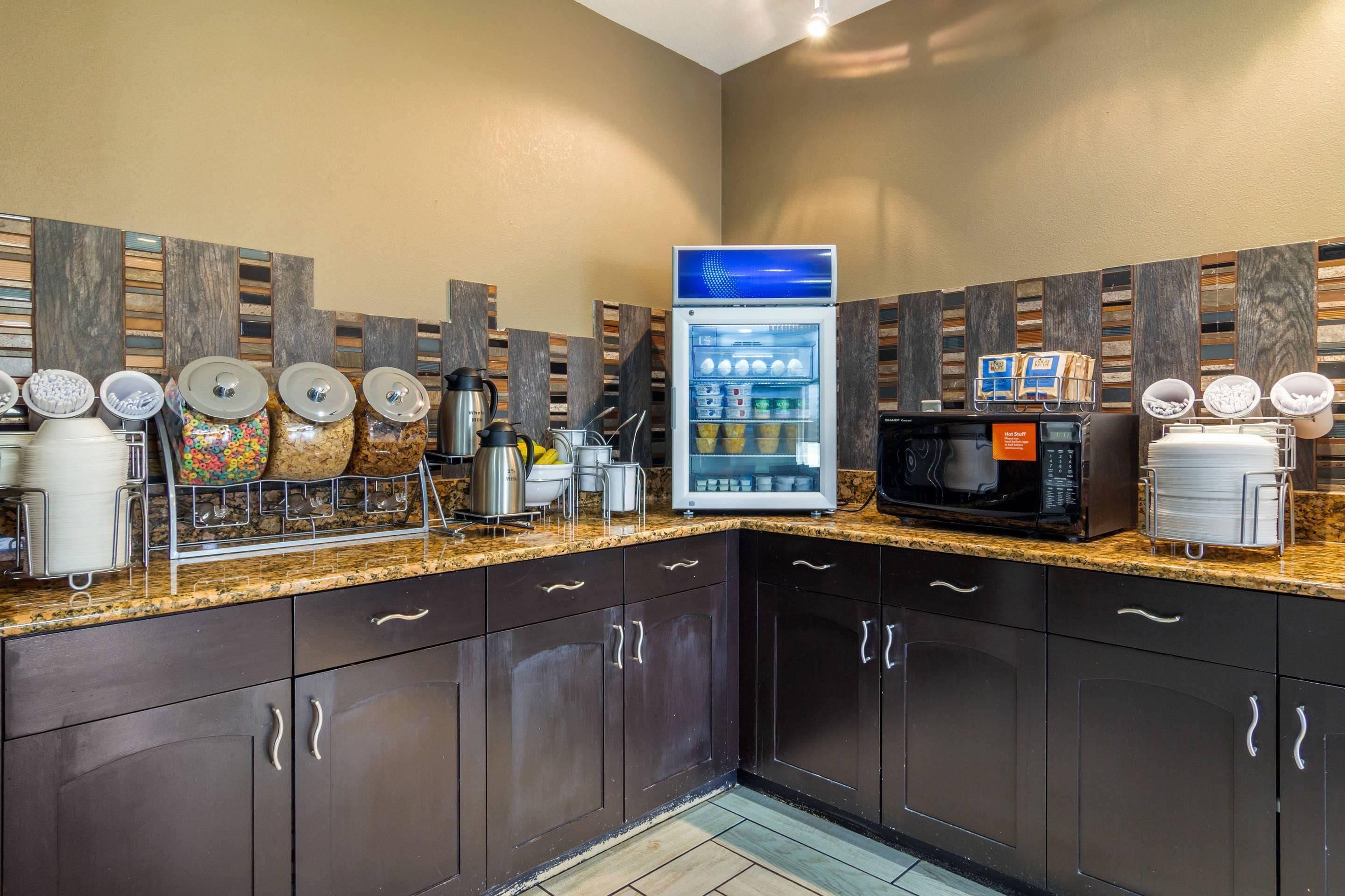A modern kitchen with dark cabinets, a granite countertop, a coffee machine, a microwave, and a beverage dispenser.