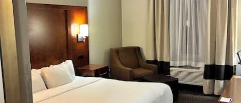 Une chambre d’hôtel avec un grand lit, une chaise, un bureau et une fenêtre avec des rideaux.