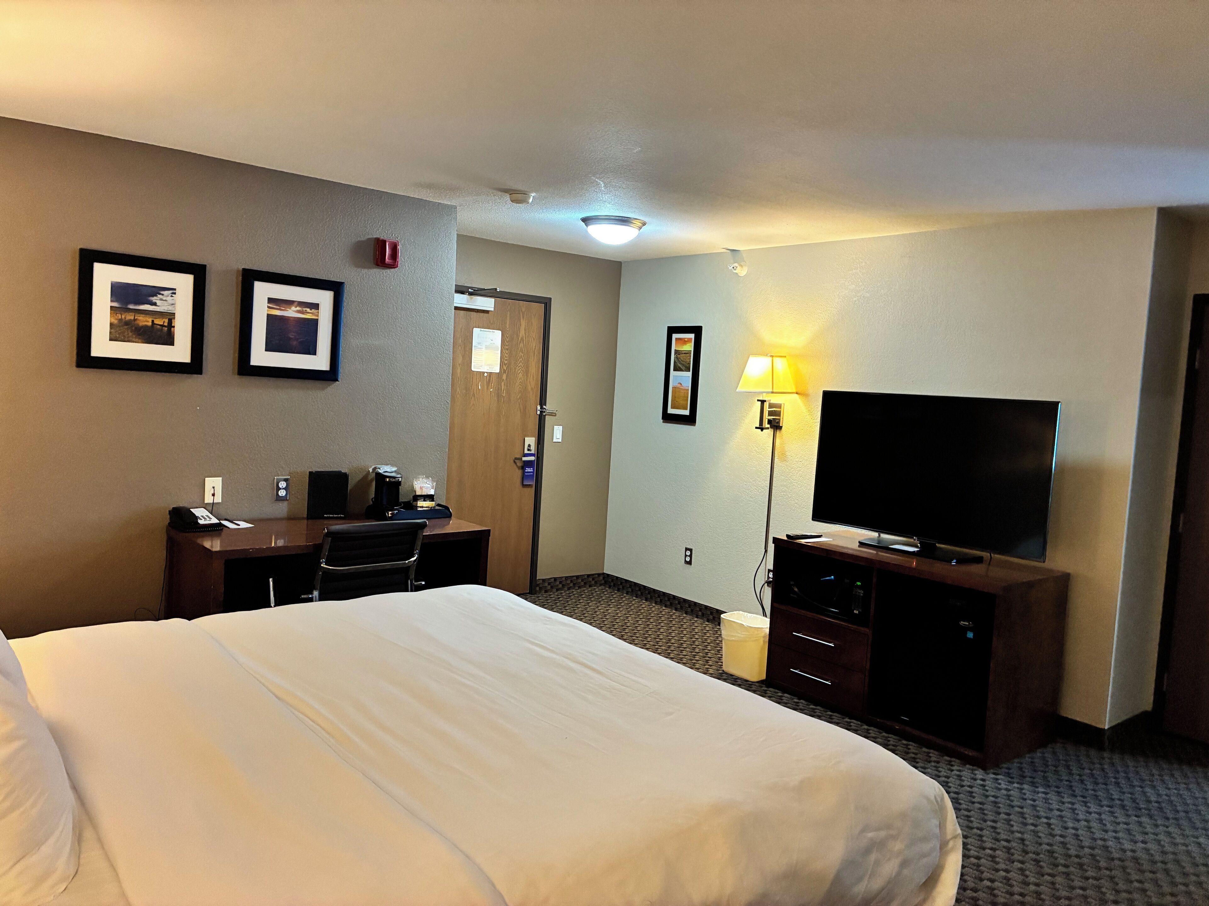 Una habitación de hotel con una cama grande, un escritorio con una computadora, un televisor y una lámpara.