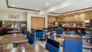 A restaurant with wooden tables and blue chairs, a bar area with a menu display, and a wall with a word cloud. - Comfort Inn & Suites Sterling (Sterling)
