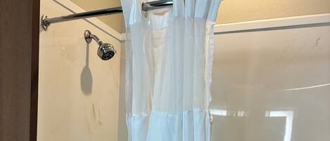 A shower area with a white curtain, a handheld showerhead, and a control panel with two buttons.