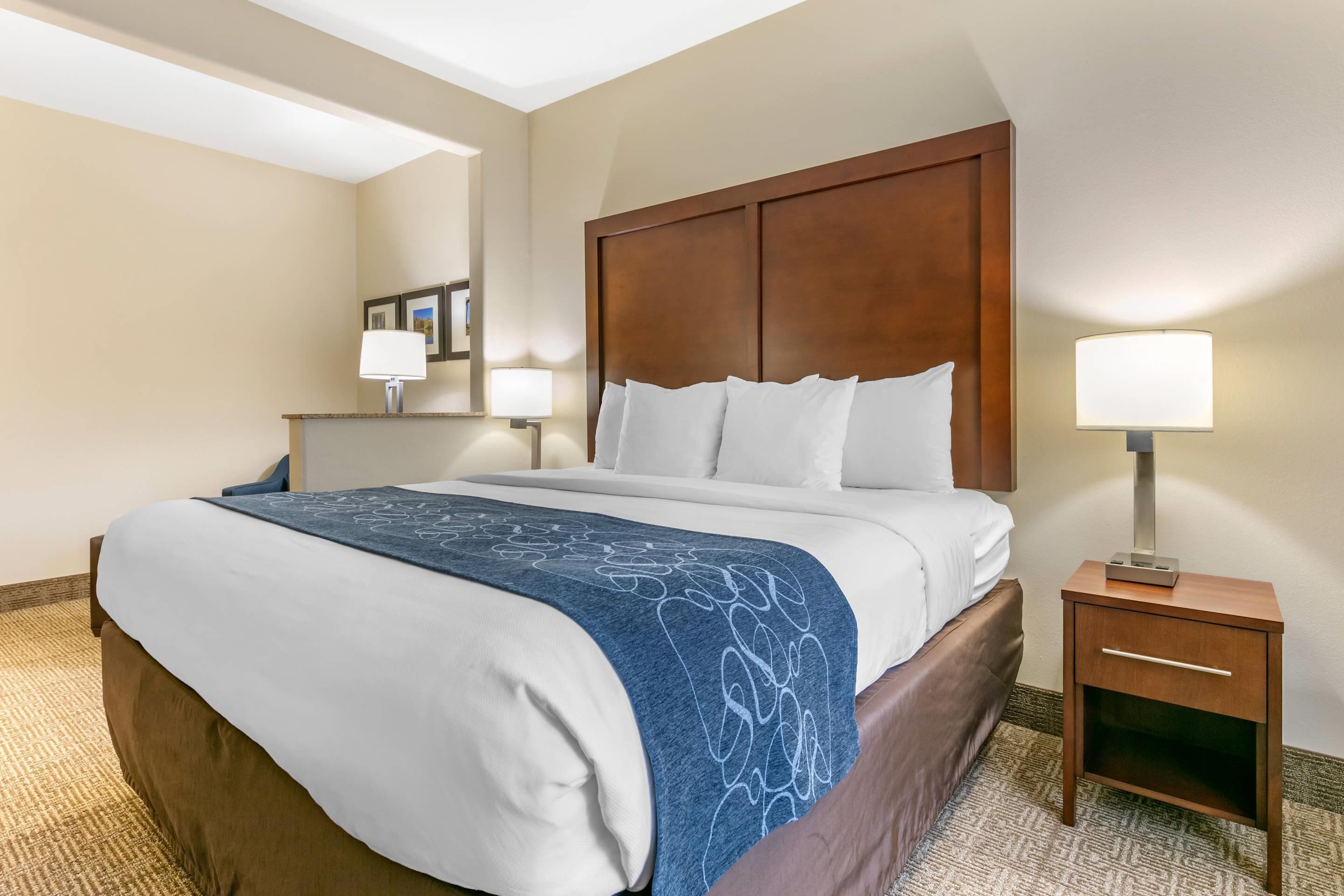 A hotel room with a bed, bedside table, lamp, and a mirror on the wall.