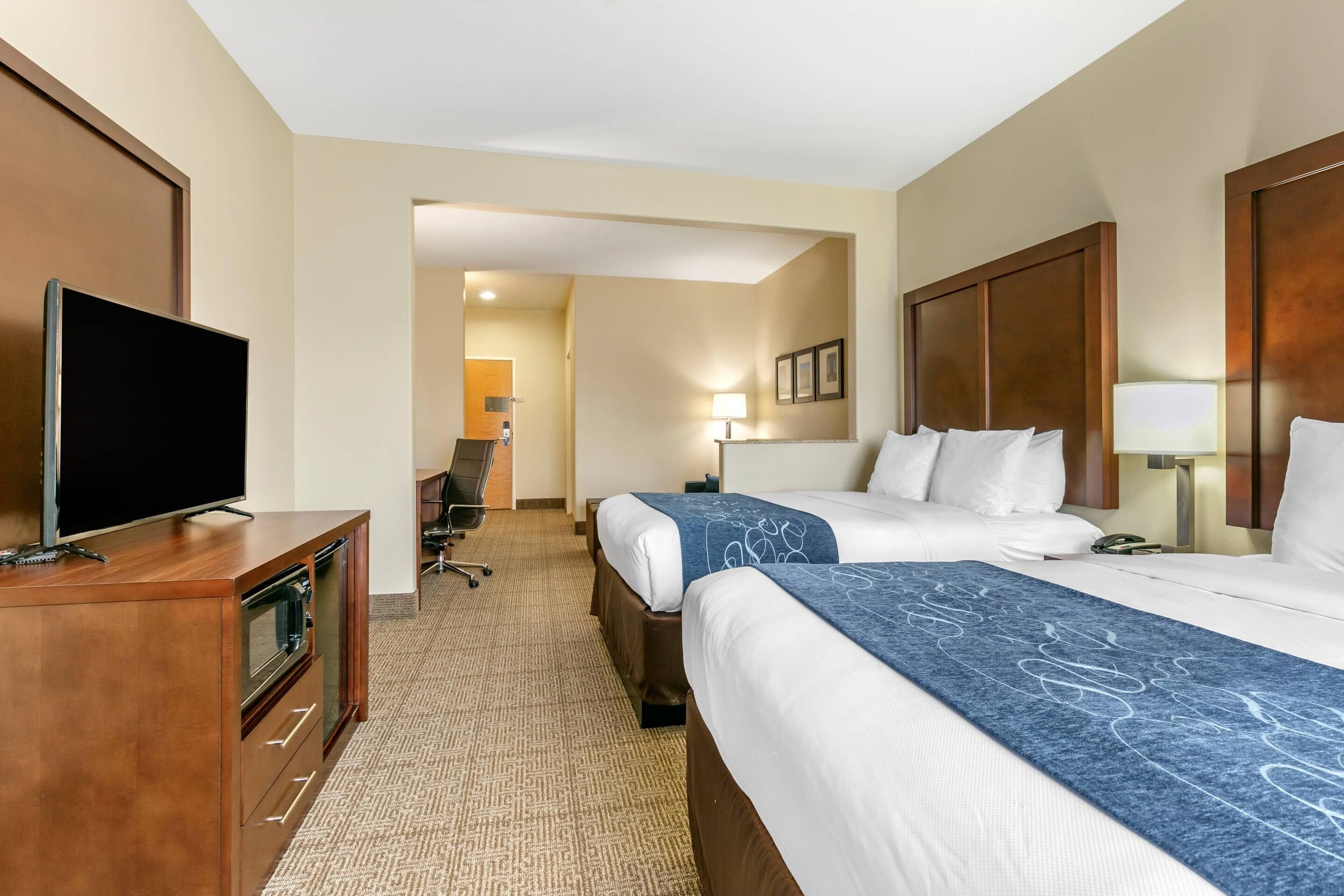 Habitación de hotel con dos camas, televisión, escritorio con televisor y piso alfombrado.