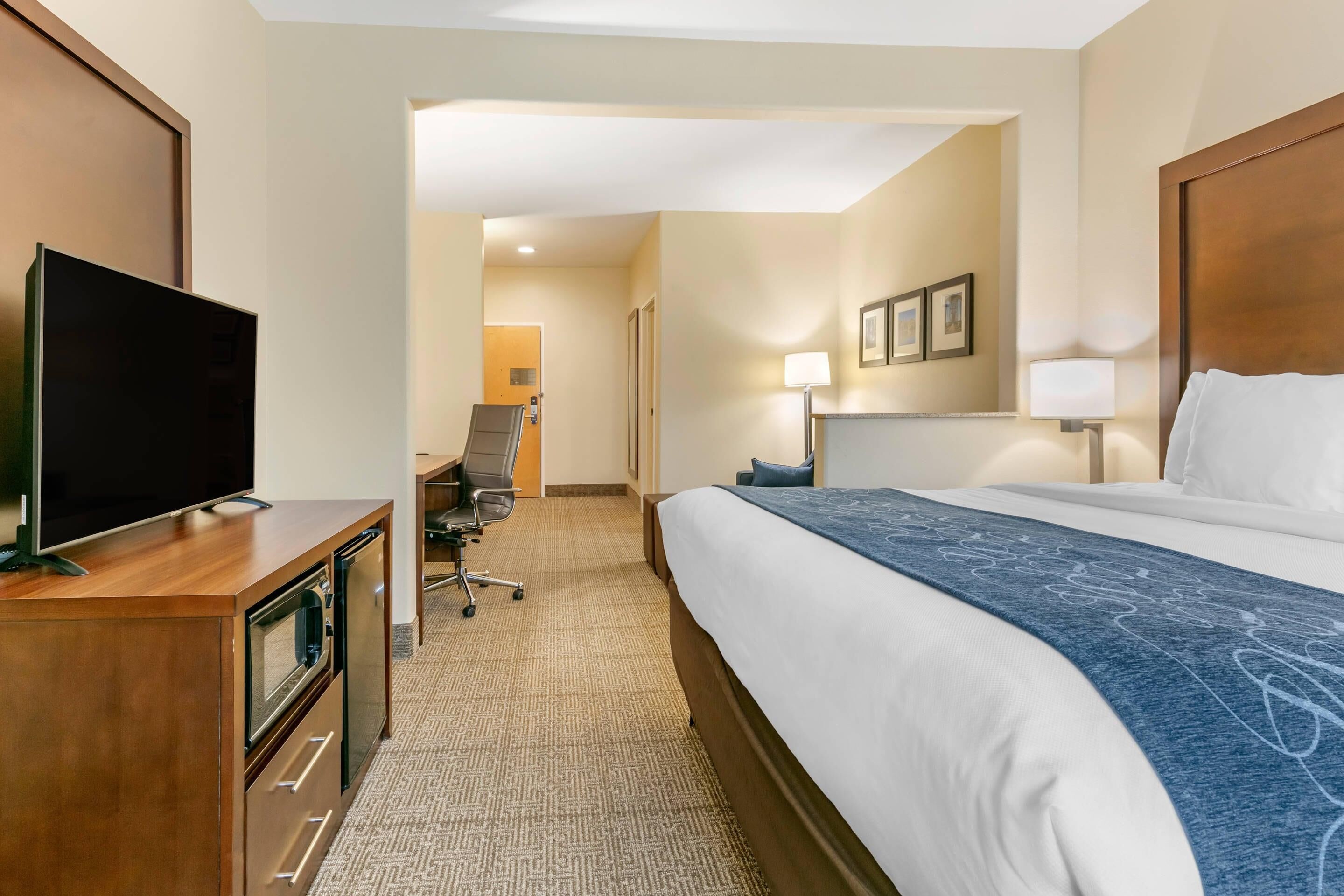 A hotel room with a bed, a TV on a wooden cabinet, a desk with a chair, and a lamp.