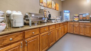 A hotel kitchen with a buffet setup, including a coffee machine, a waffle maker, and a refrigerated display. - Comfort Suites Batesville (Batesville)