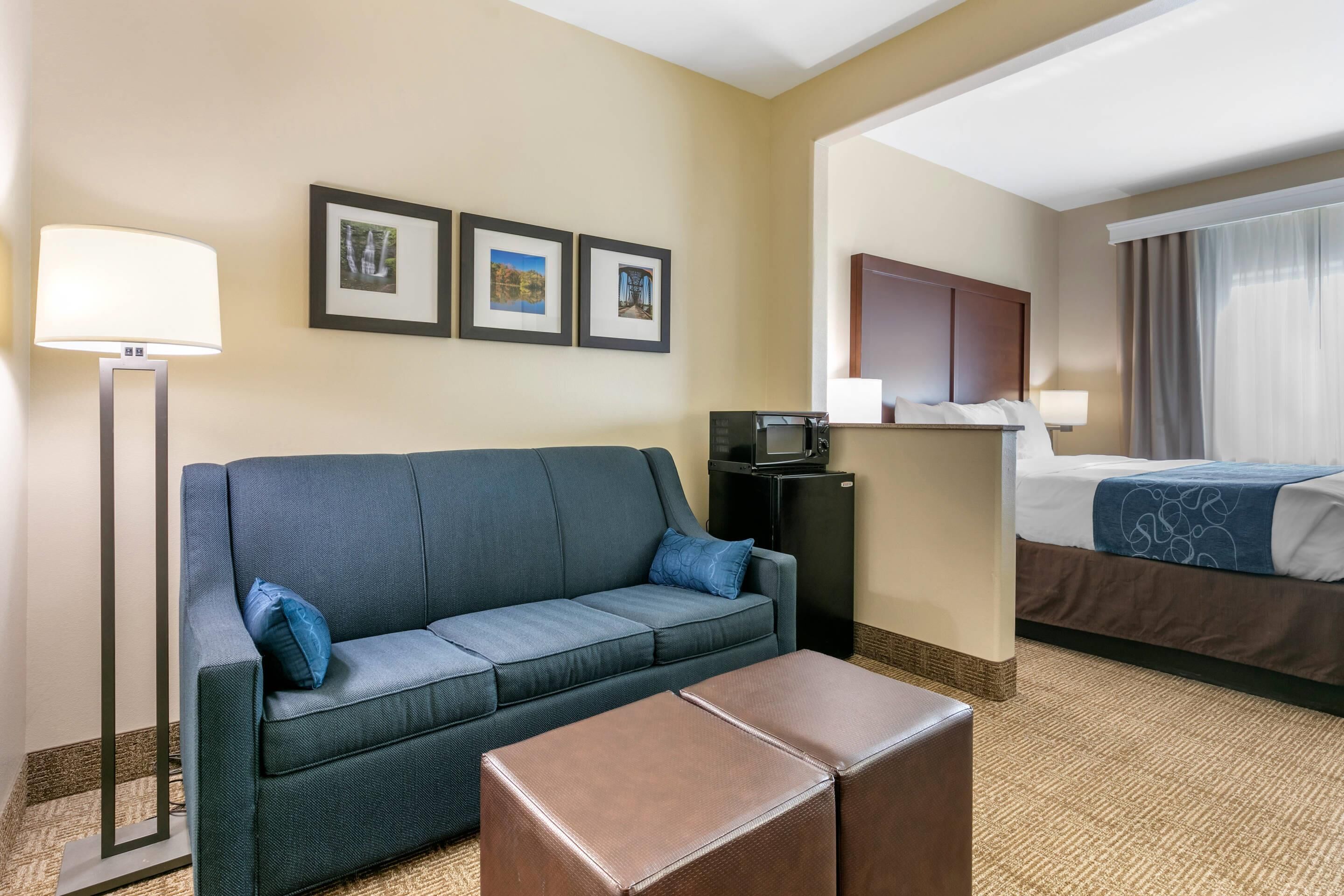 A hotel room with a sofa, a coffee table, a bed, a desk with a computer, and framed pictures on the wall.