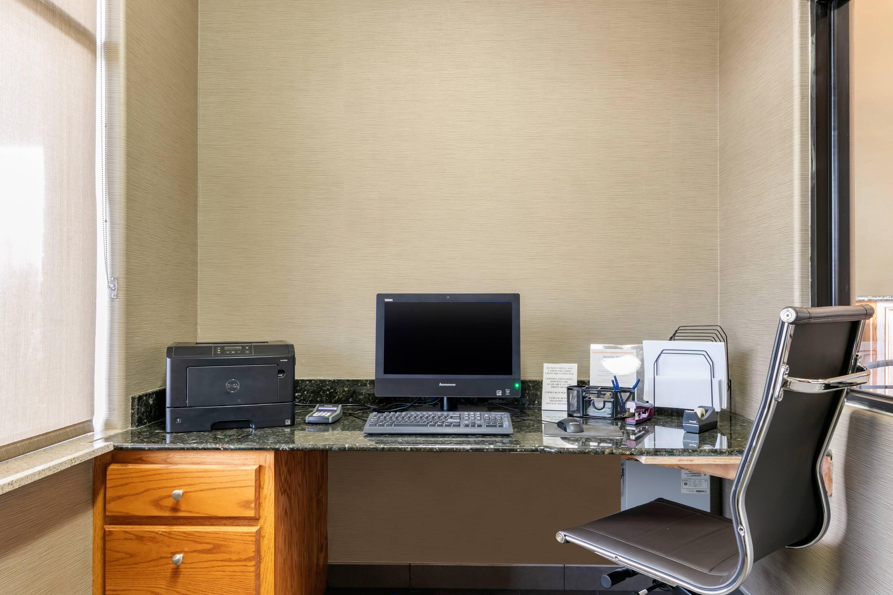 Ein kleiner Arbeitsraum mit Schreibtischcomputer, Drucker, Tastatur und Stuhl.