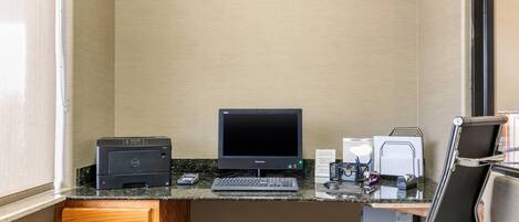 A small office with a desktop computer, printer, keyboard, and a chair.
