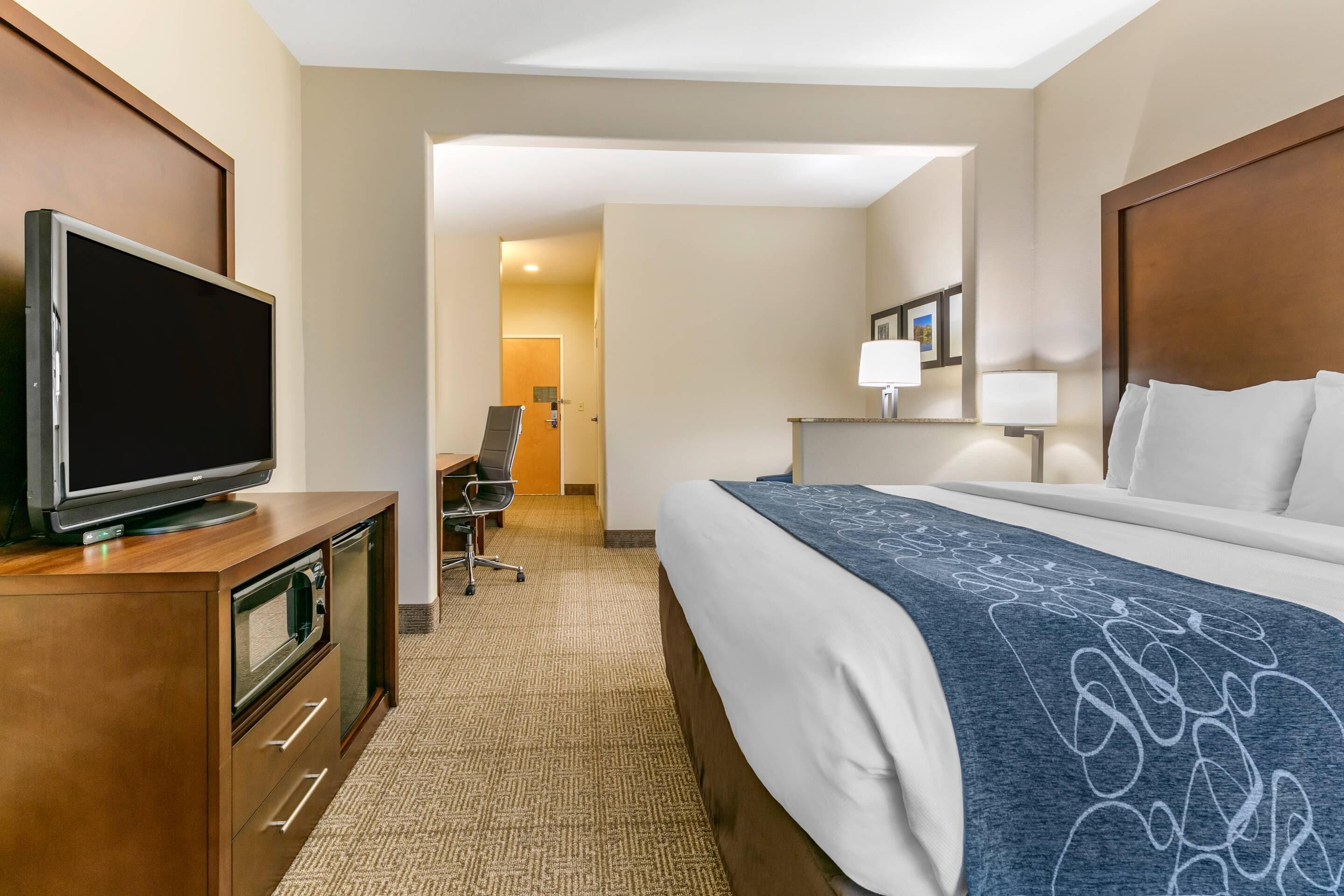 A hotel room with a bed, a TV on a wooden cabinet, a desk with a chair, and a lamp.
