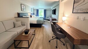 A hotel room with a bed, a desk, a chair, a sofa, and a TV.