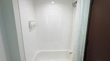 Un baño con azulejos blancos, ducha e inodoro.