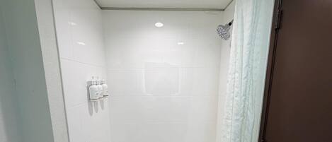 Une salle de bain avec des carreaux blancs, une douche et des toilettes.
