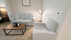 A modern living room with a sofa, a coffee table, a floor lamp, and a wall-mounted thermostat.
