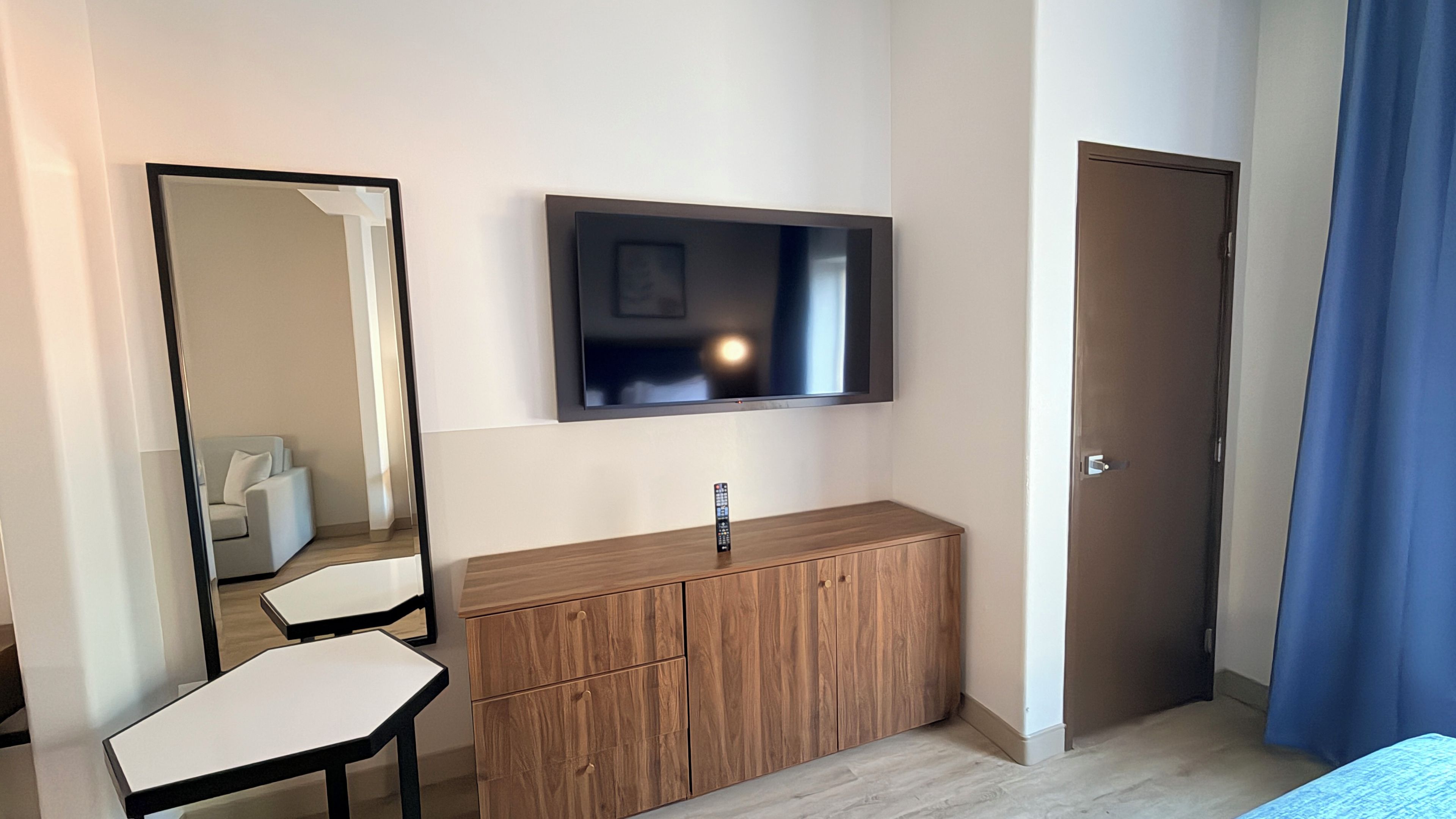 A hotel room with a bed, a TV mounted on the wall, a wooden dresser, a mirror, and a door.