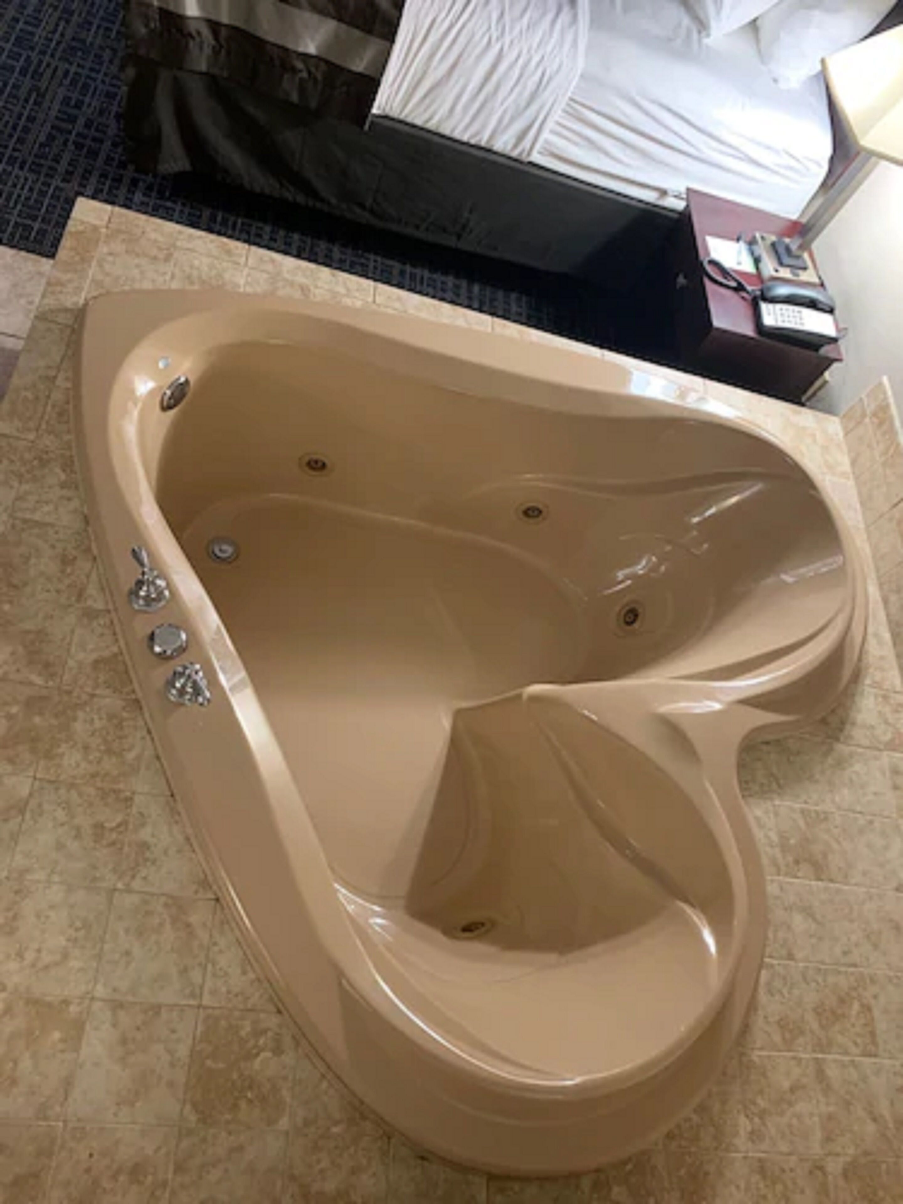 A large, beige, freestanding bathtub in a hotel room with a tiled floor.