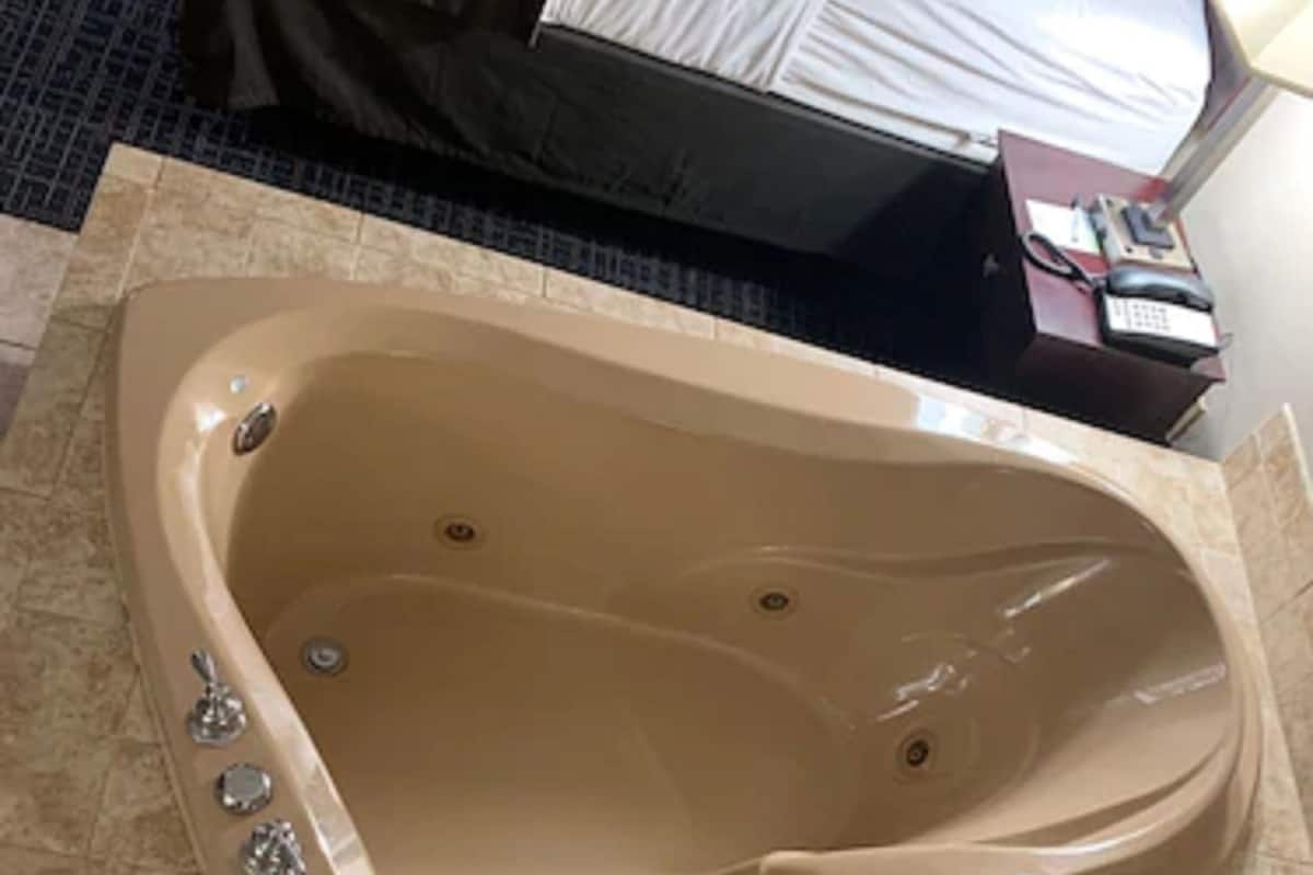 A large, beige, freestanding bathtub in a hotel room with a tiled floor.