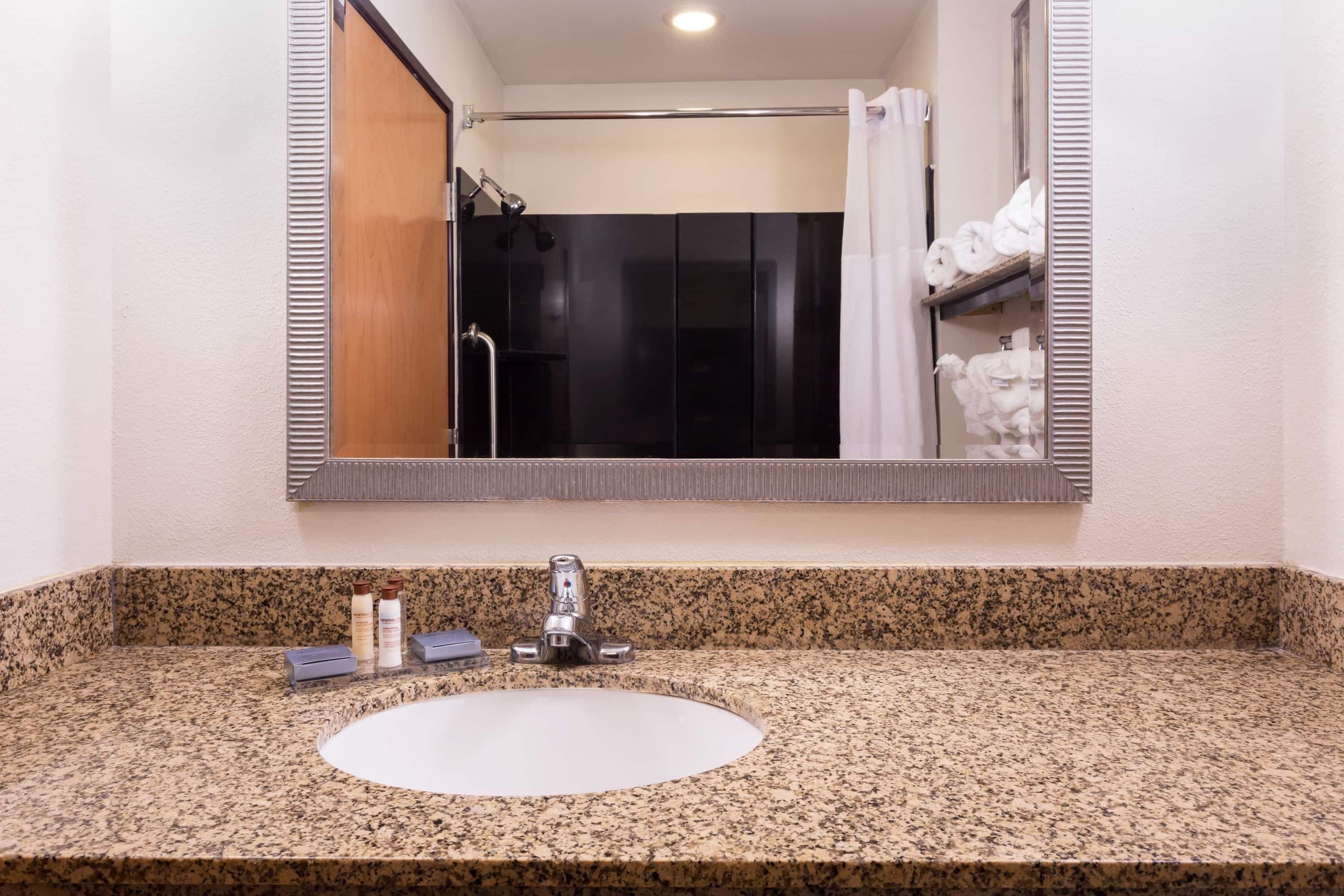 A bathroom with a granite countertop, a sink, a mirror, and a shower visible in the reflection.