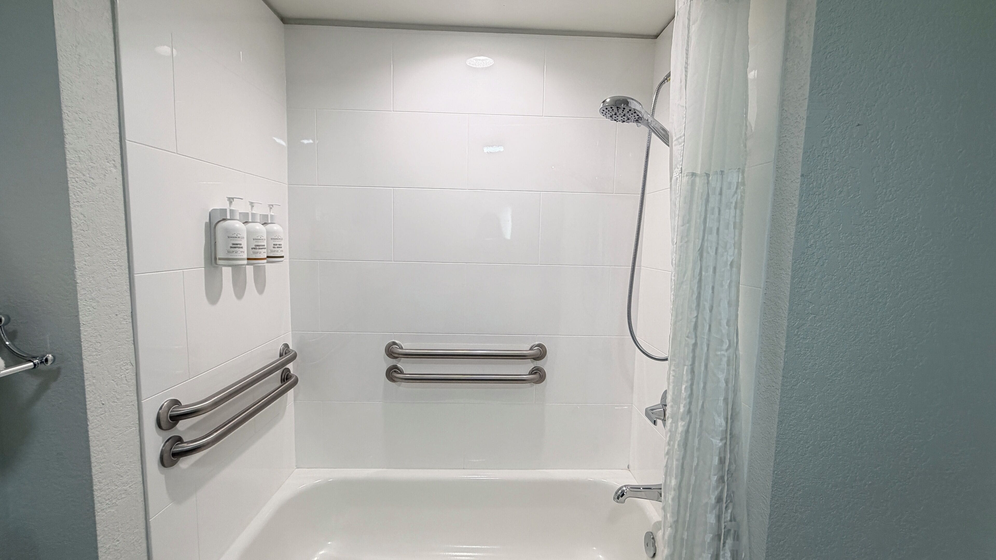 A walk-in shower with white tiles, a handheld showerhead, and grab bars.