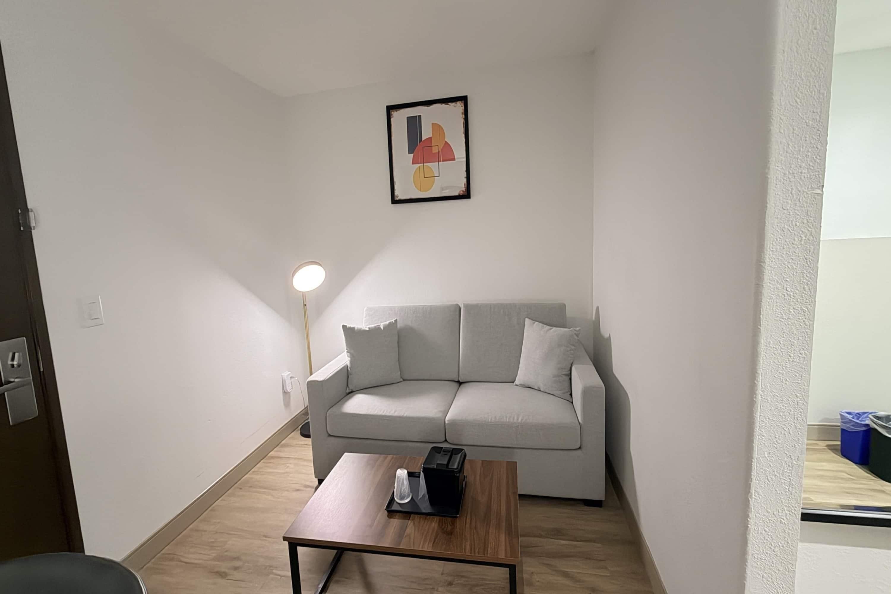 A small, modern living room with a grey sofa, a wooden coffee table, and a floor lamp.