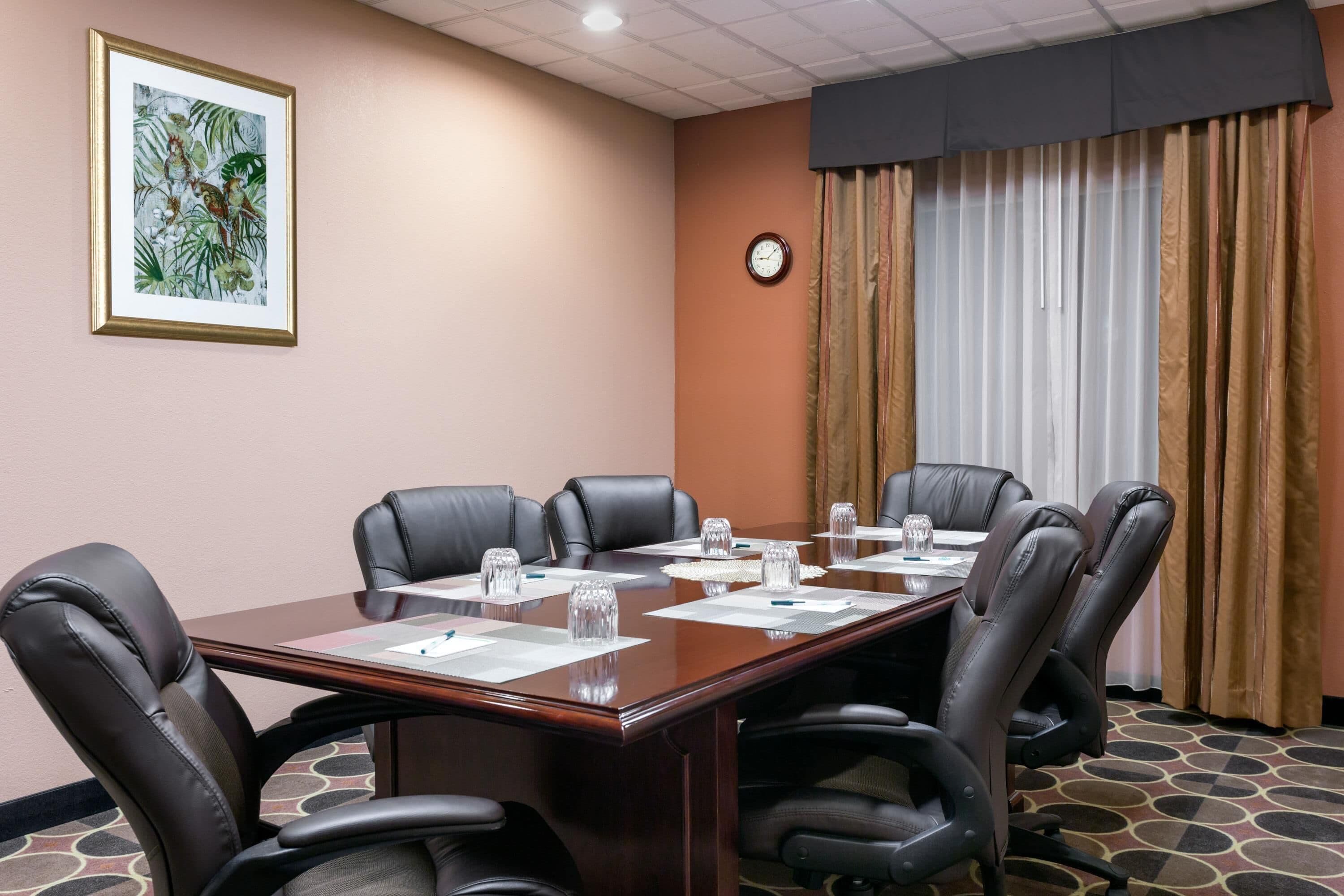 A conference room with a long table, black leather chairs, a clock, and a framed picture on the wall.
