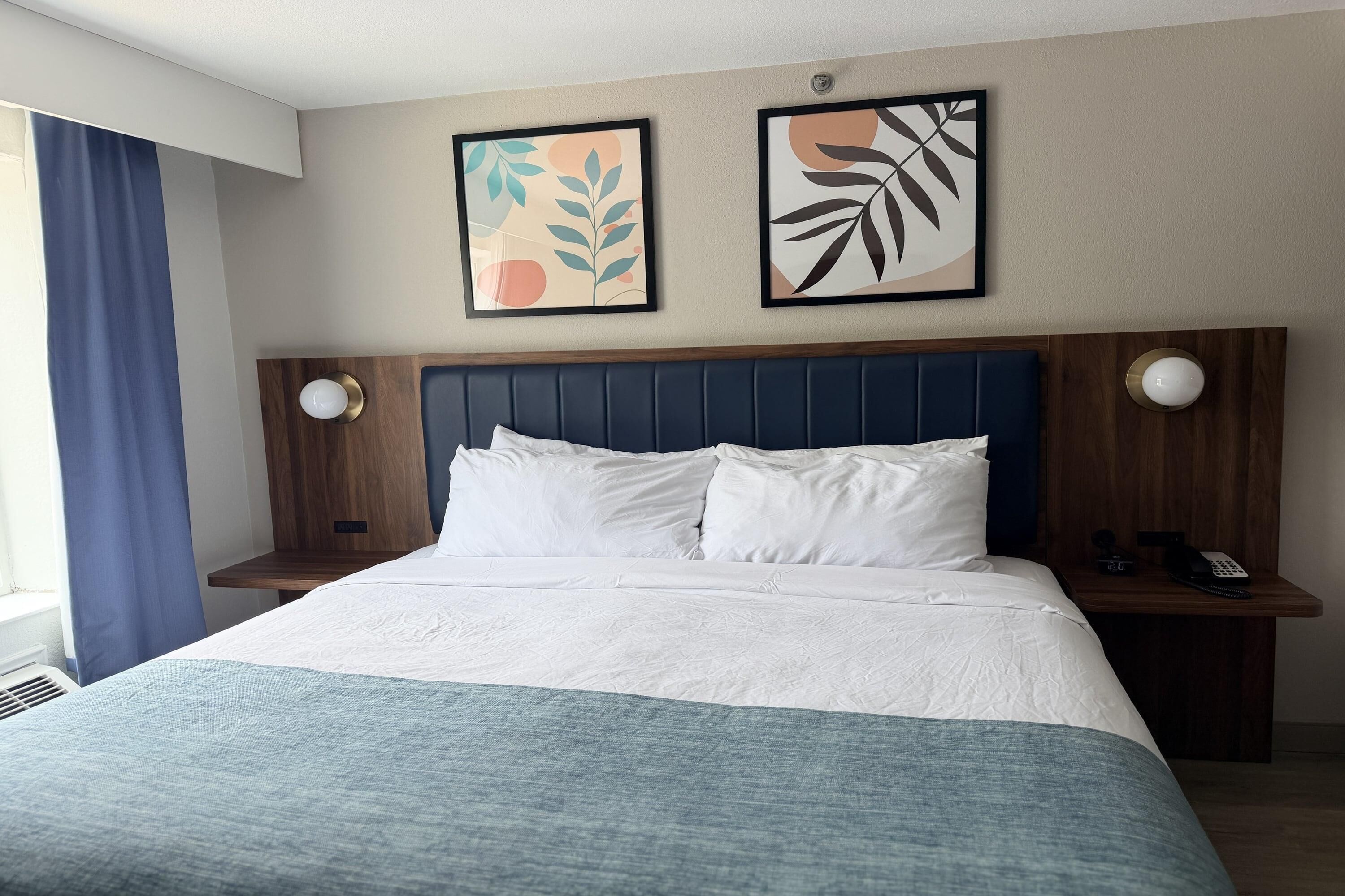 A hotel room with a bed, two nightstands, a telephone, and artwork on the wall.